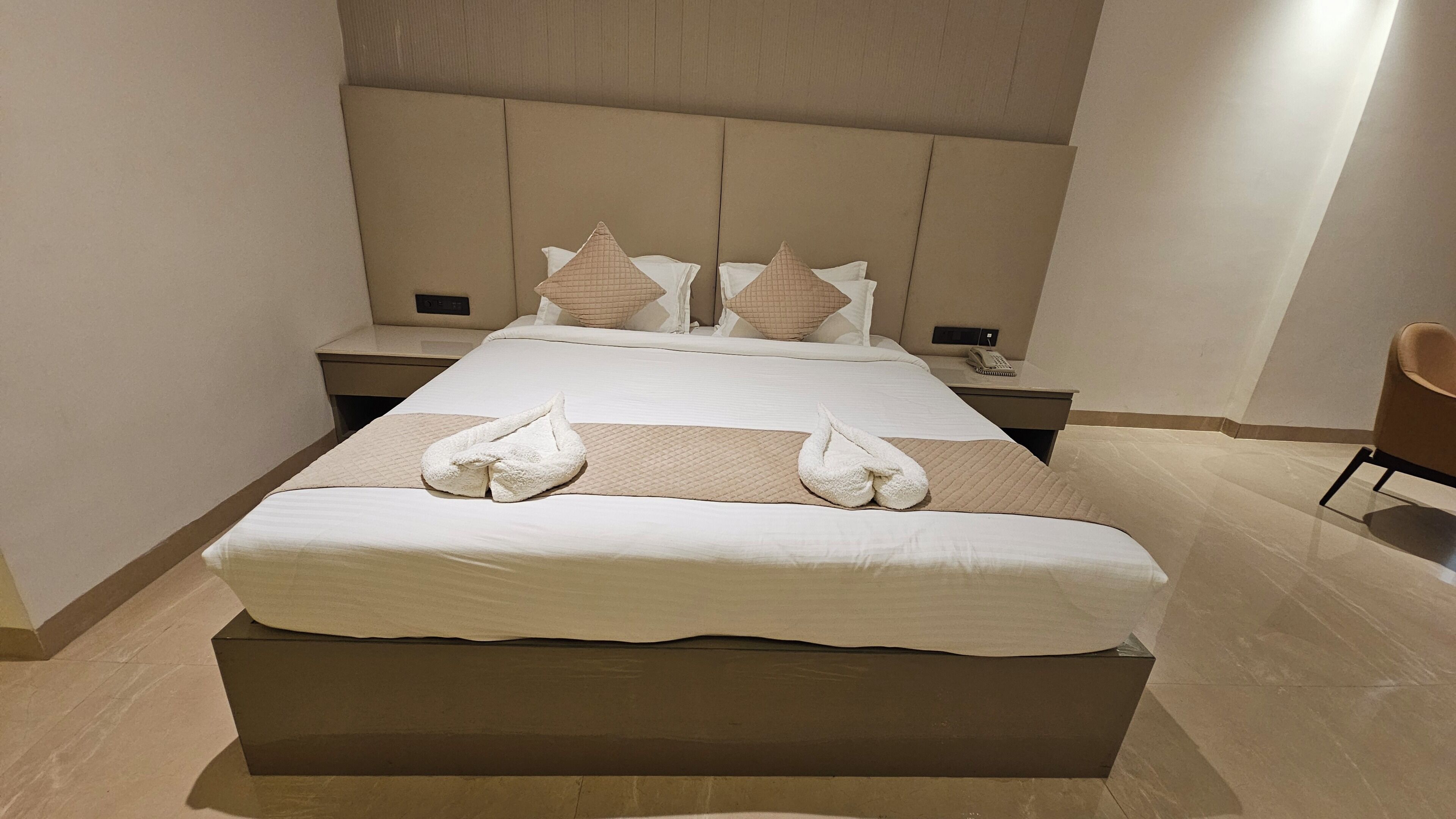 Une chambre d’hôtel avec un grand lit, deux tables de chevet, une chaise et une petite table de nuit avec un téléphone.