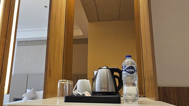Habitación de hotel con tocador de madera, espejo, hervidor de agua, botella de agua y taza.