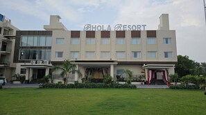 Un hôtel appelé « BHOLA RESORT », doté d’une architecture moderne, comprenant plusieurs étages, une entrée principale agrémentée d’éléments décoratifs et une pelouse bien entretenue à l’avant.
