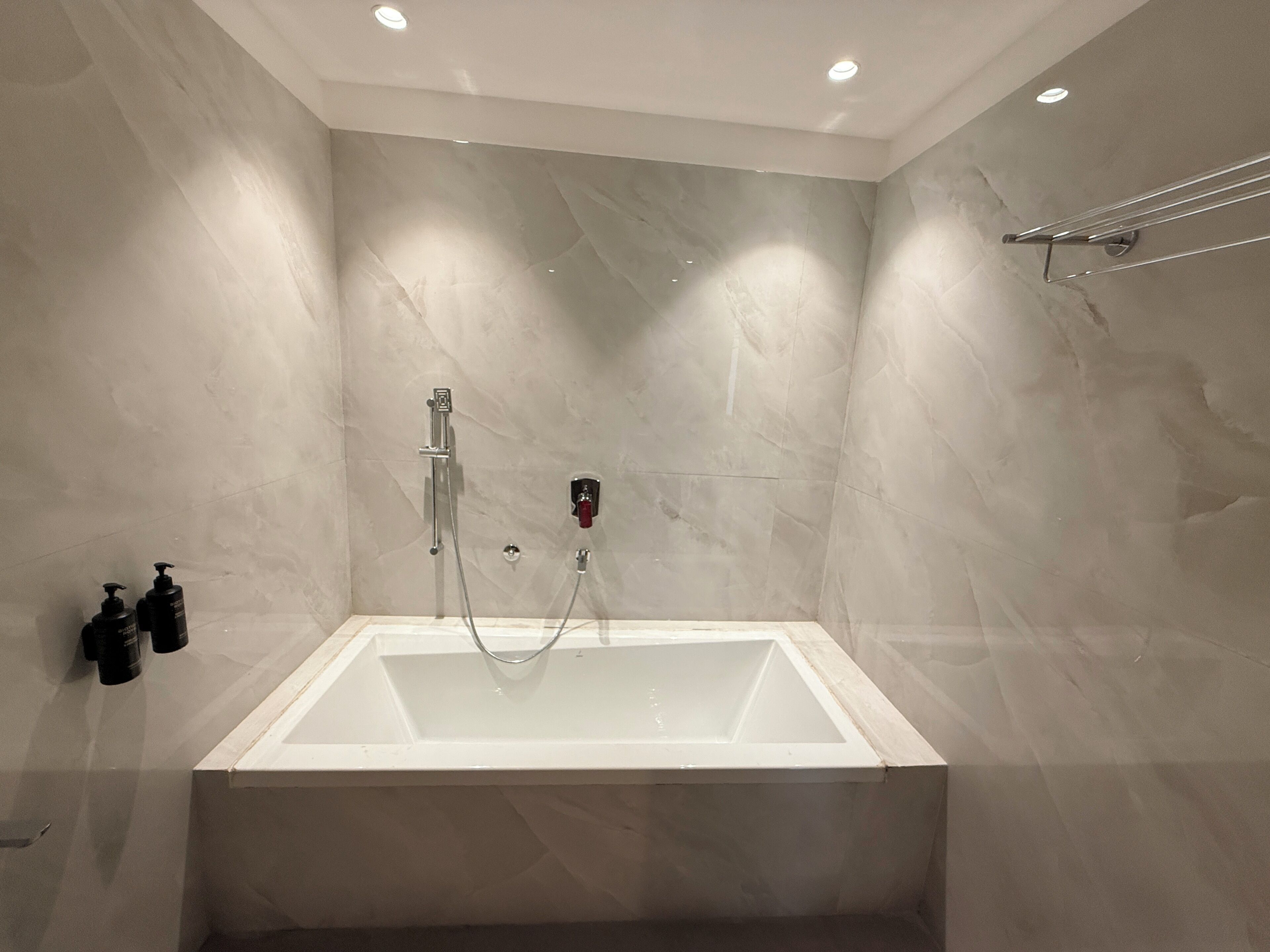 Un baño moderno con una bañera rectangular, un cabezal de ducha de mano y un perchero de toallas en la pared.