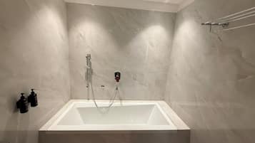 Un baño moderno con una bañera rectangular, un cabezal de ducha de mano y un perchero de toallas en la pared.