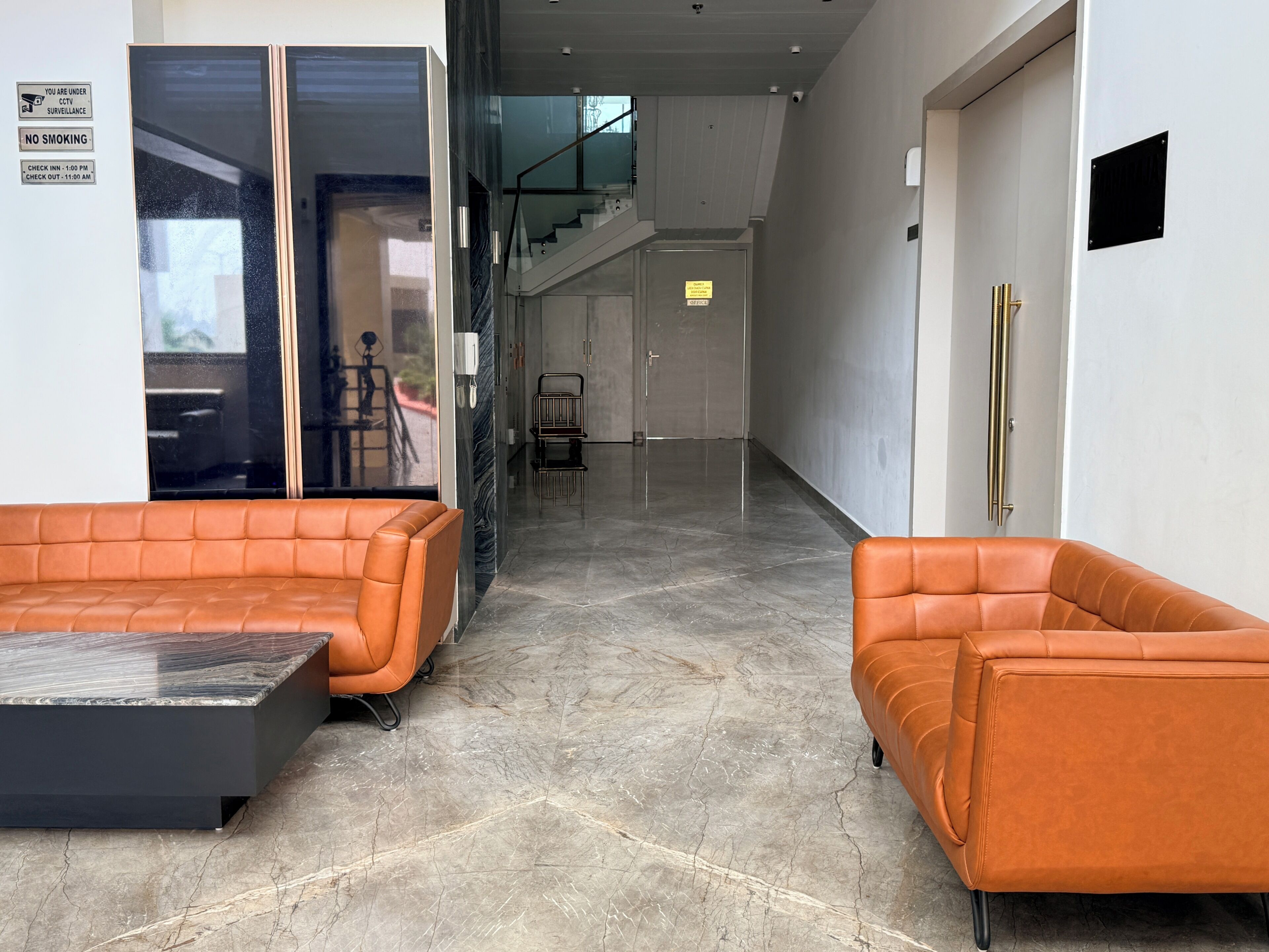Een moderne lobby met een receptiebalie, een zithoek en een trap.