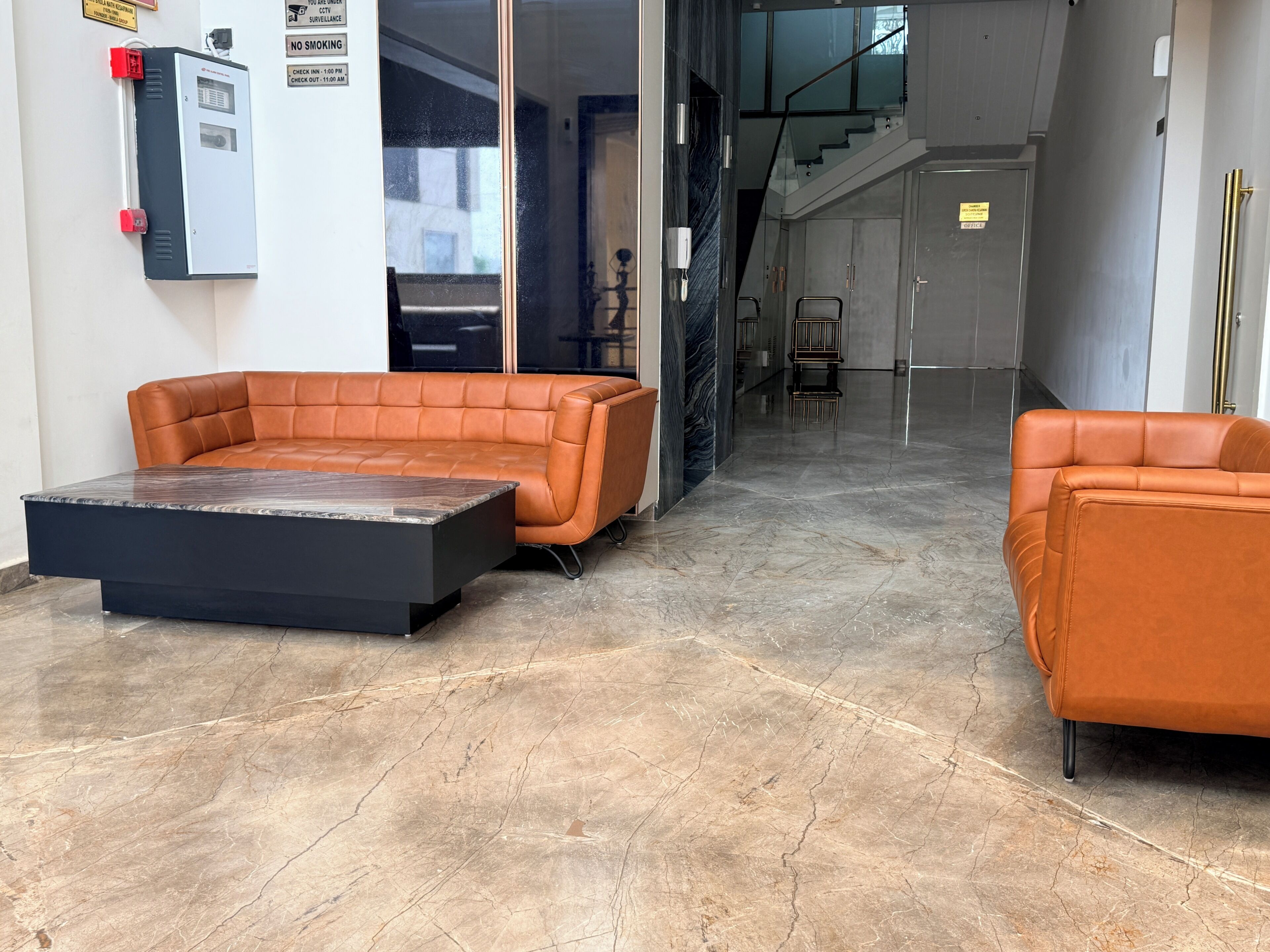 A modern lobby with a leather sofa, a marble coffee table, and a staircase leading to an upper floor.