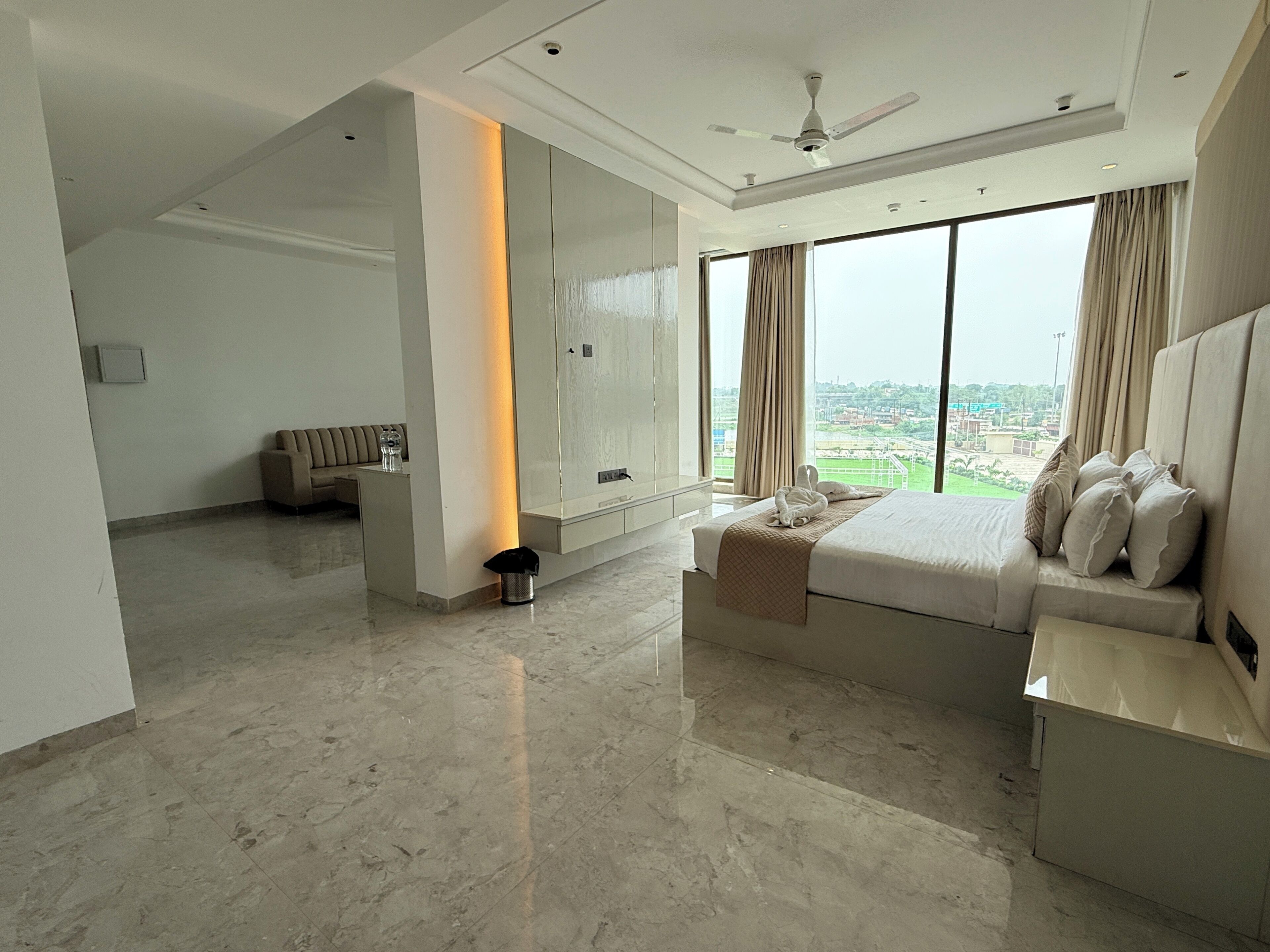 A modern hotel room with a large bed, a seating area, and a view of the city.