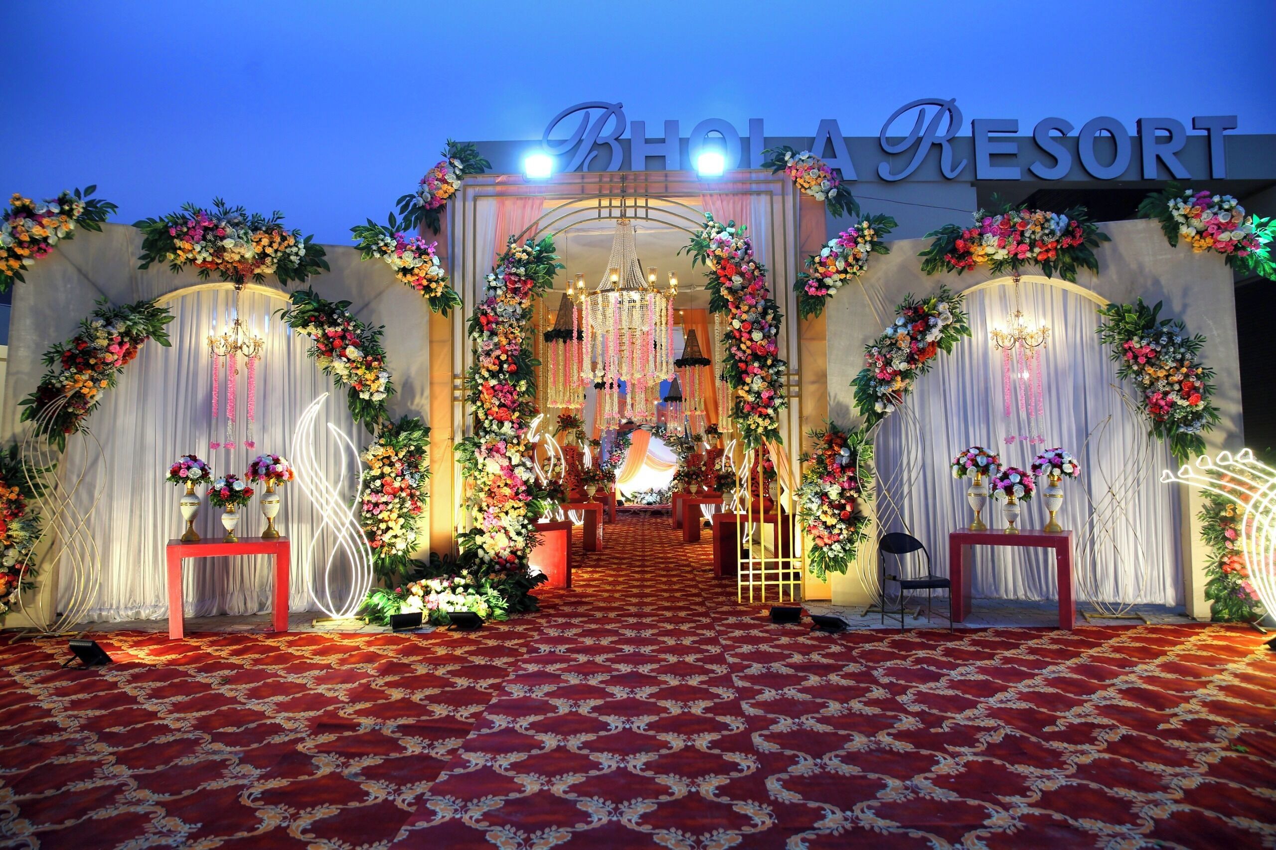 A decorated entrance to a venue with a red carpet, floral arrangements, and a chandelier.