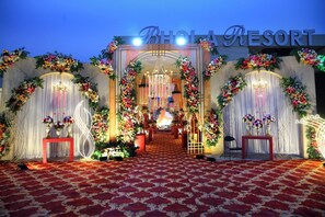 Une entrée décorée, avec un tapis rouge, des compositions florales et un lustre, menant à un lieu de réception.