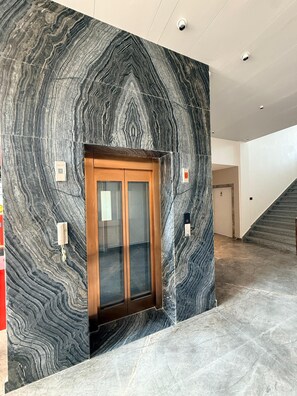 Un interior moderno con una pared de mármol, un ascensor de madera y una escalera.