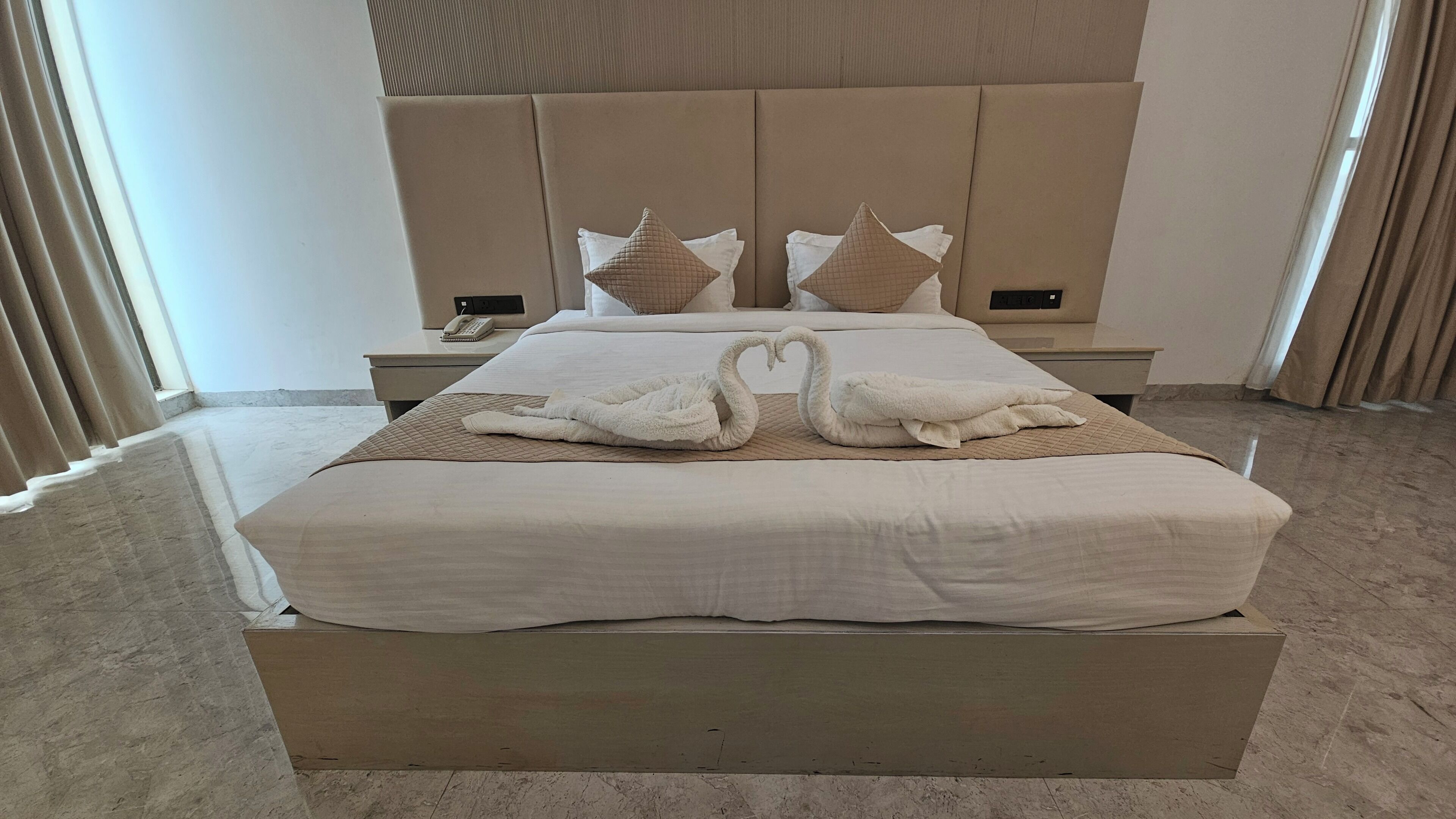 A hotel room with a large bed, a bedside table with a phone, and a headboard with decorative pillows.