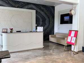 Un mostrador de recepción con una computadora, un reloj y un letrero rojo.
