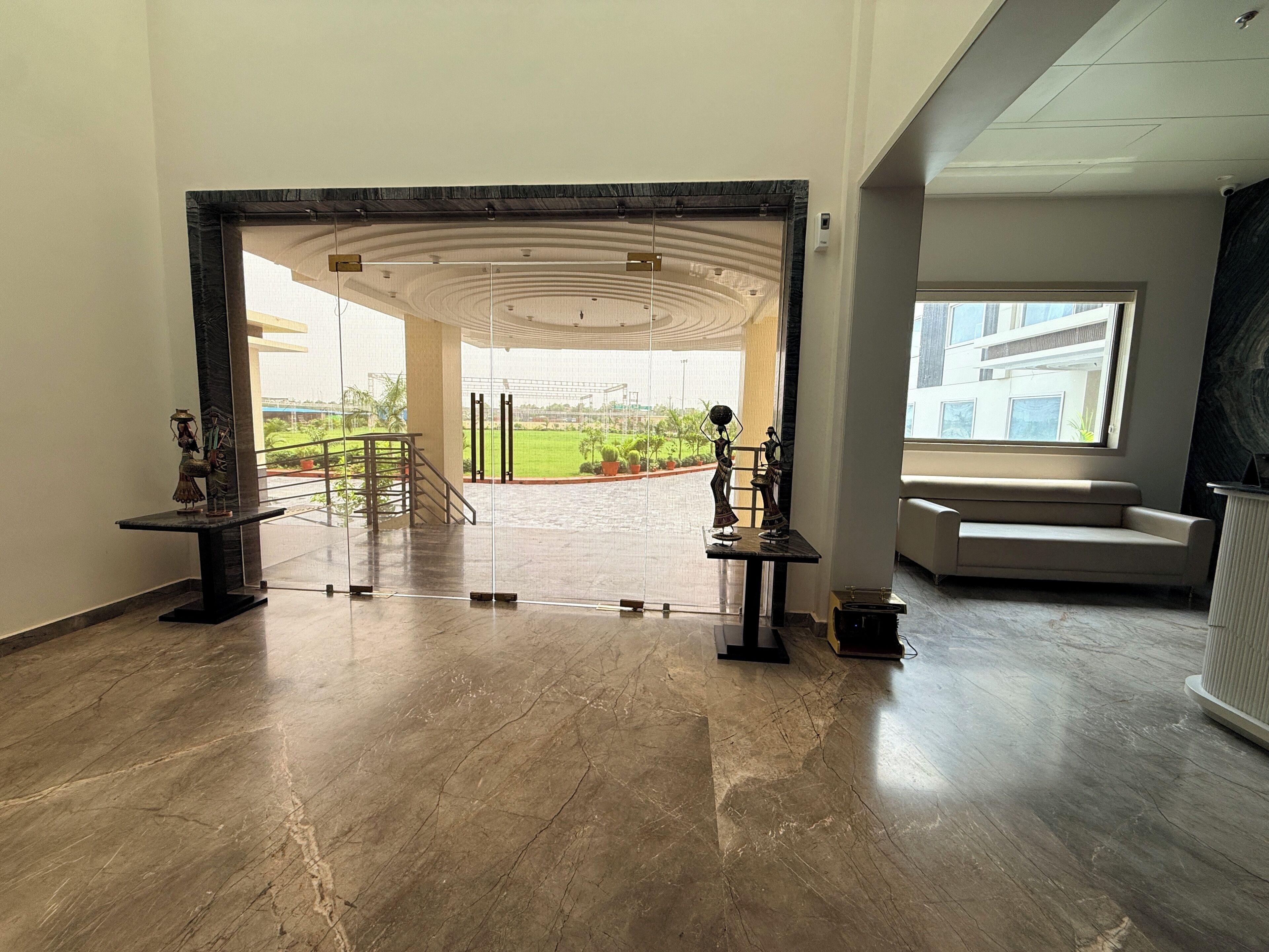 A spacious lobby with a marble floor, a central staircase, and a view of a landscaped area outside.