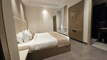 A modern hotel room with a large bed, a bedside table, a mirror, and a wardrobe.