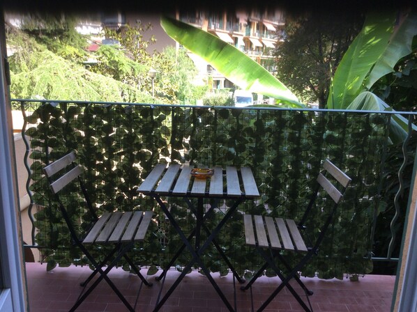 Ein Balkon mit Tisch und Stühlen, umgeben von einer grünen, blätterreichen Abschirmung.
