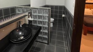 Un baño pequeño con un lavabo negro, inodoro y zona de ducha.