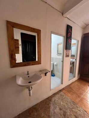 Un baño con lavamanos, espejo y puerta que da a la zona de la ducha.