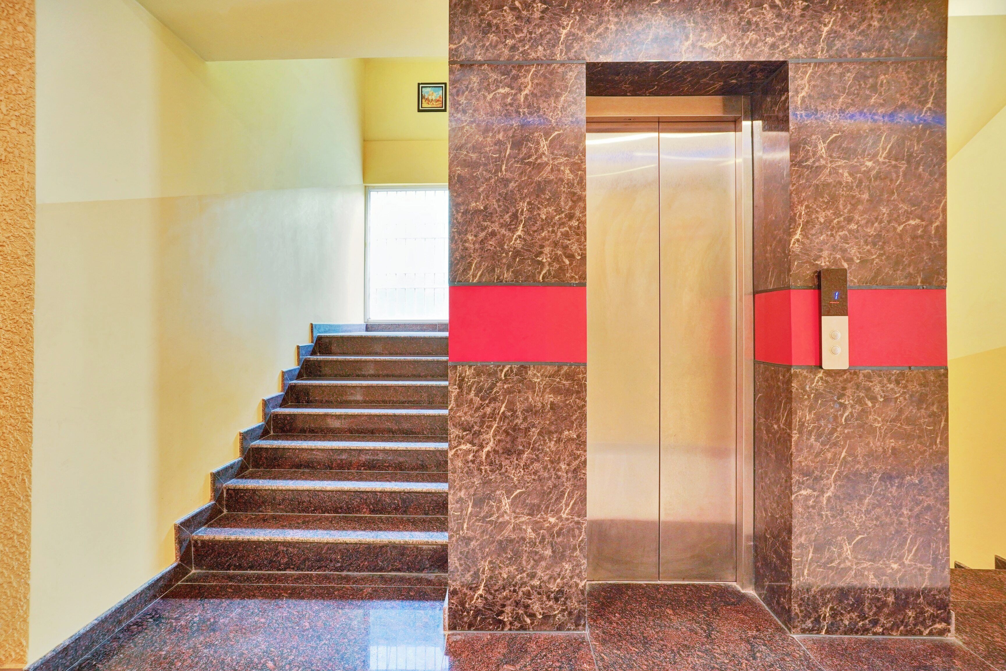 A staircase leading to an elevator with marble walls and a red accent.