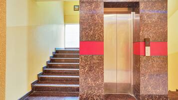 A staircase leading to an elevator with marble walls and a red accent.