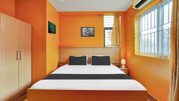A hotel room with a bed, a wardrobe, a ceiling fan, a window with curtains, and a picture on the wall.