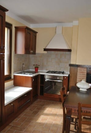 A kitchen with wooden cabinets, a gas stove, a sink, and a tiled backsplash. - "The Infinity" Apartment of Sibillini Montains (Montefortino)