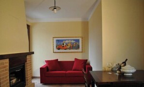 A living room with a red sofa, a painting on the wall, a fireplace, and a dining table with glasses and a bottle. - "The Infinity" Apartment of Sibillini Montains (Montefortino)