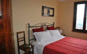 A single bed with a red quilt, a wooden chair, and a window with a view. - "The Infinity" Apartment of Sibillini Montains (Montefortino)