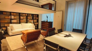A modern living room with a white sofa, a dining table with chairs, a bookshelf, and a radiator. - Loft, a designer apartment in a prime downtown location (Milano)