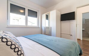 Ein Schlafzimmer mit einem Bett, einem Fenster, einer Tür und einem an der Wand befestigten Fernseher.