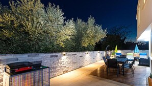 En udendørs terrasse med en stenvæg, grill og siddepladser.