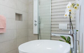 Ein Badezimmer mit einem weißen Waschbecken, einer Duschkabine aus Glas und einer Orchidee im Topf.
