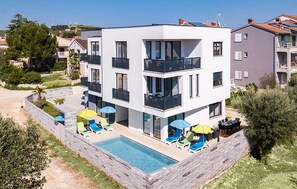 A modern multi-story building with a swimming pool, outdoor seating, and a stone retaining wall. - Luxurious apartment in Medulin with WiFi (Medulin)