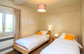 Une chambre avec deux lits en bois, une fenêtre avec des rideaux et des œuvres d’art mural.