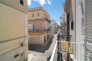 Un carrer estret amb edificis a banda i banda, cel clar i una barana metàl·lica a la dreta.