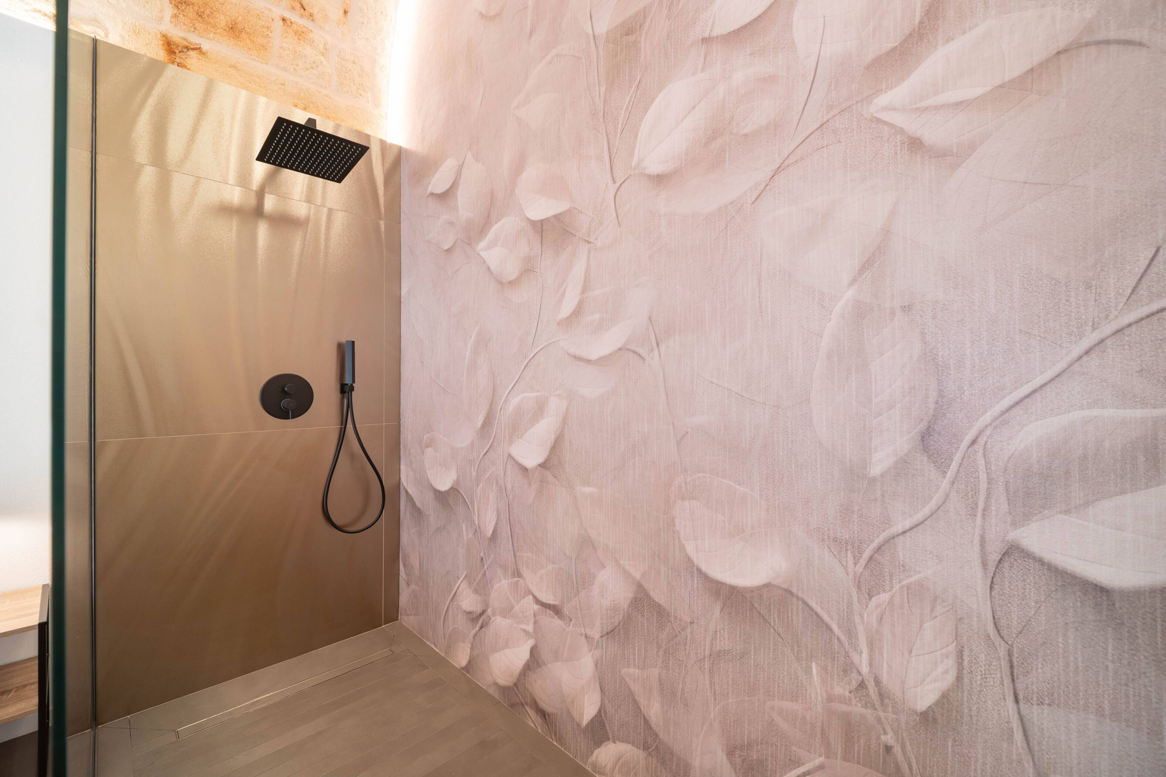 A shower with a transparent door, a handheld showerhead, and a wall with a leaf pattern.
