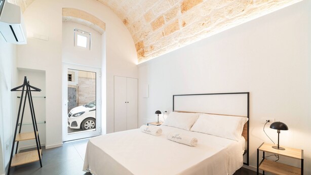 Ein Hotelzimmer mit Bett, Schreibtisch, Lampe und Blick auf ein Auto durch eine Tür.