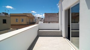 Ein Balkon mit Blick auf benachbarte Gebäude, eine Tür mit Fenster und ein kleiner Tritt zur Erde.