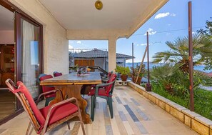 Eine Terrasse im Freien mit Holztisch und -stühlen, Blick aufs Meer und einem Gebäude im Hintergrund.