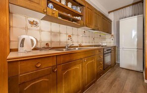 Eine Küche mit Holzschränken, einem weißen Kühlschrank und einer gefliesten Spritzschutzwand.