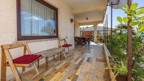 Un balcón con una banca de madera, una mesa de comedor con sillas y plantas en macetas.