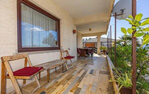 Ein Balkon mit einer Holzbank, einem Esstisch mit Stühlen und Topfpflanzen.