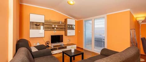 Una sala de estar con sofá, mesa de centro, televisor y puerta corrediza de vidrio que da a un balcón.