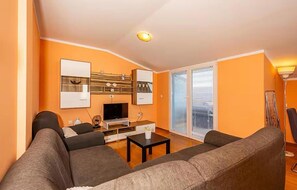 Ein Wohnzimmer mit einer Couch, einem Couchtisch, einem Fernseher und einer Schiebetür zum Balkon.