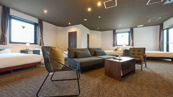 A hotel room with a bed, sofa, armchair, and a small wooden table.