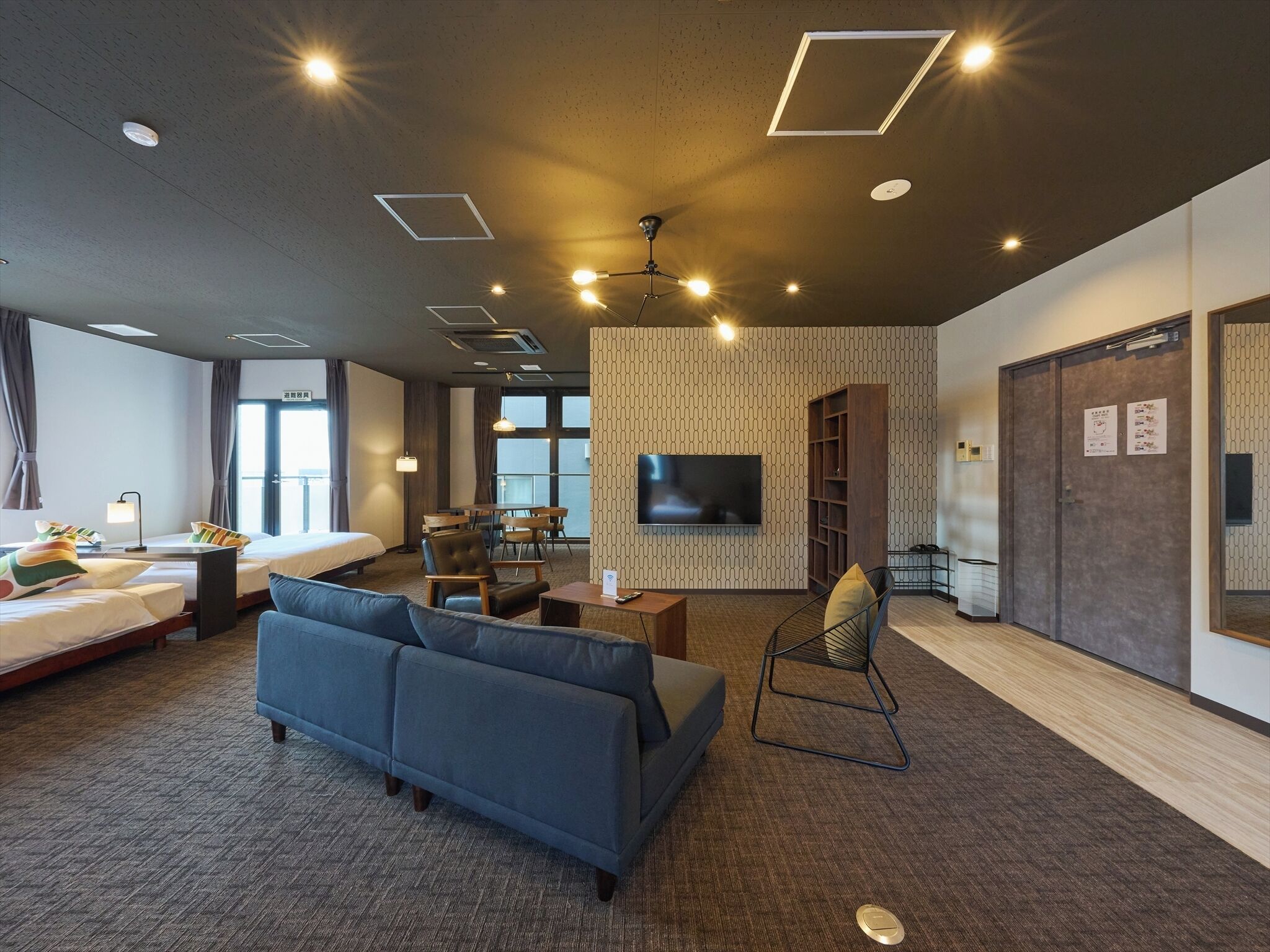 A hotel room with a large bed, a sofa, a TV, and a seating area with a chair and a small table.