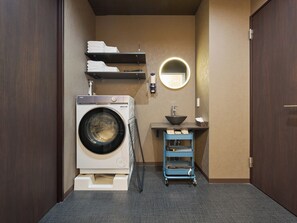 A compact laundry room with a front-loading washer, a sink, a mirror, and storage shelves. - Retrospect Stay Kannai 7 (Naka-ku, Yokohama-shi)