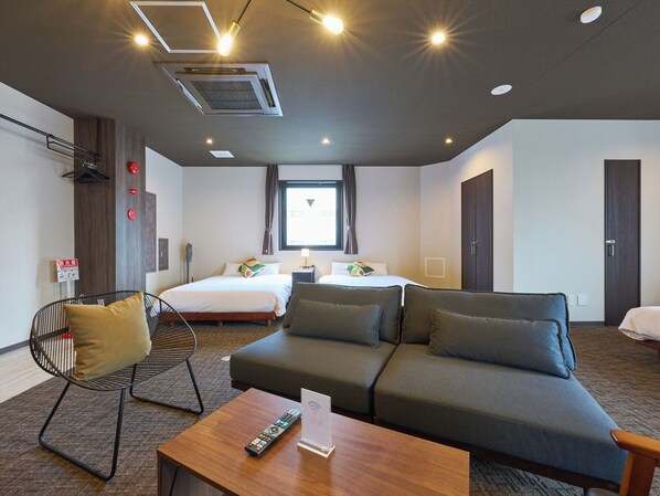 Habitación de hotel con sofá, dos camas, una silla, una mesa con control remoto y una ventana.