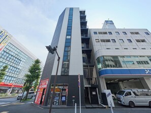 A multi-story building with a modern architectural design, featuring a prominent vertical element and a ground-level entrance with signage.