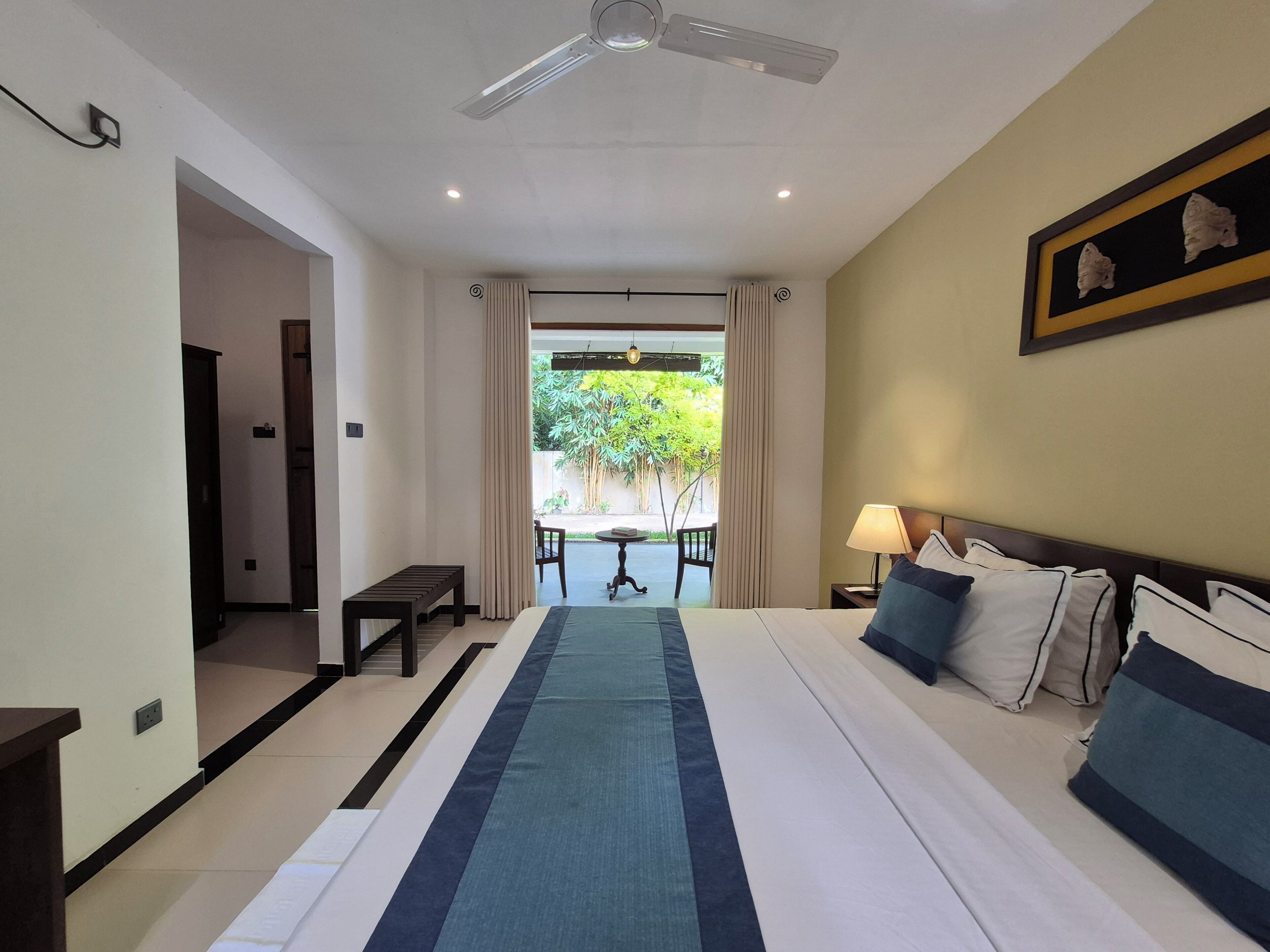 Habitación de hotel con cama, mesita de noche, lámpara y vistas al exterior.
