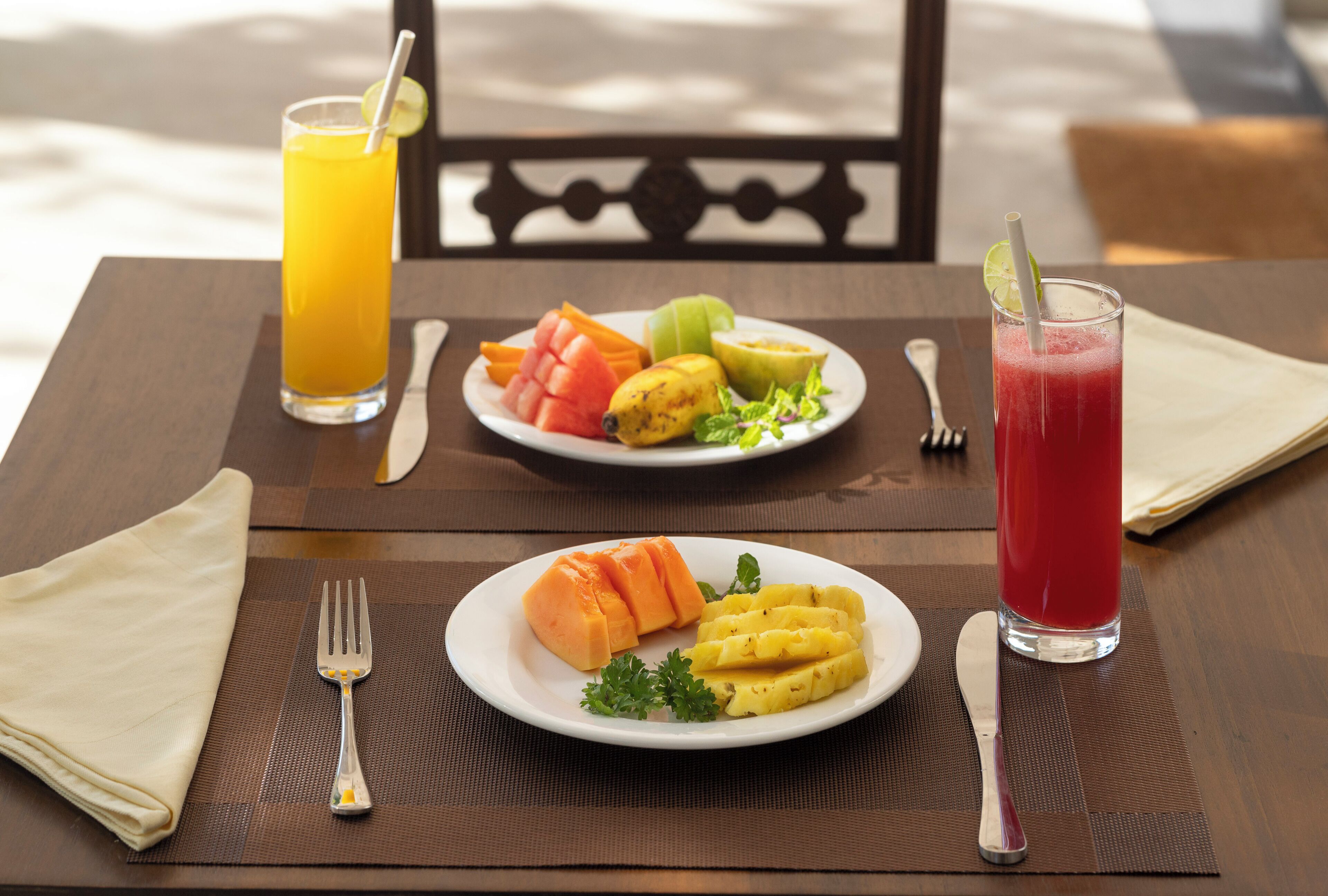 A table set with a meal, including a plate of mashed potatoes and a fruit salad, a glass of orange juice, and a glass of red drink with a straw.