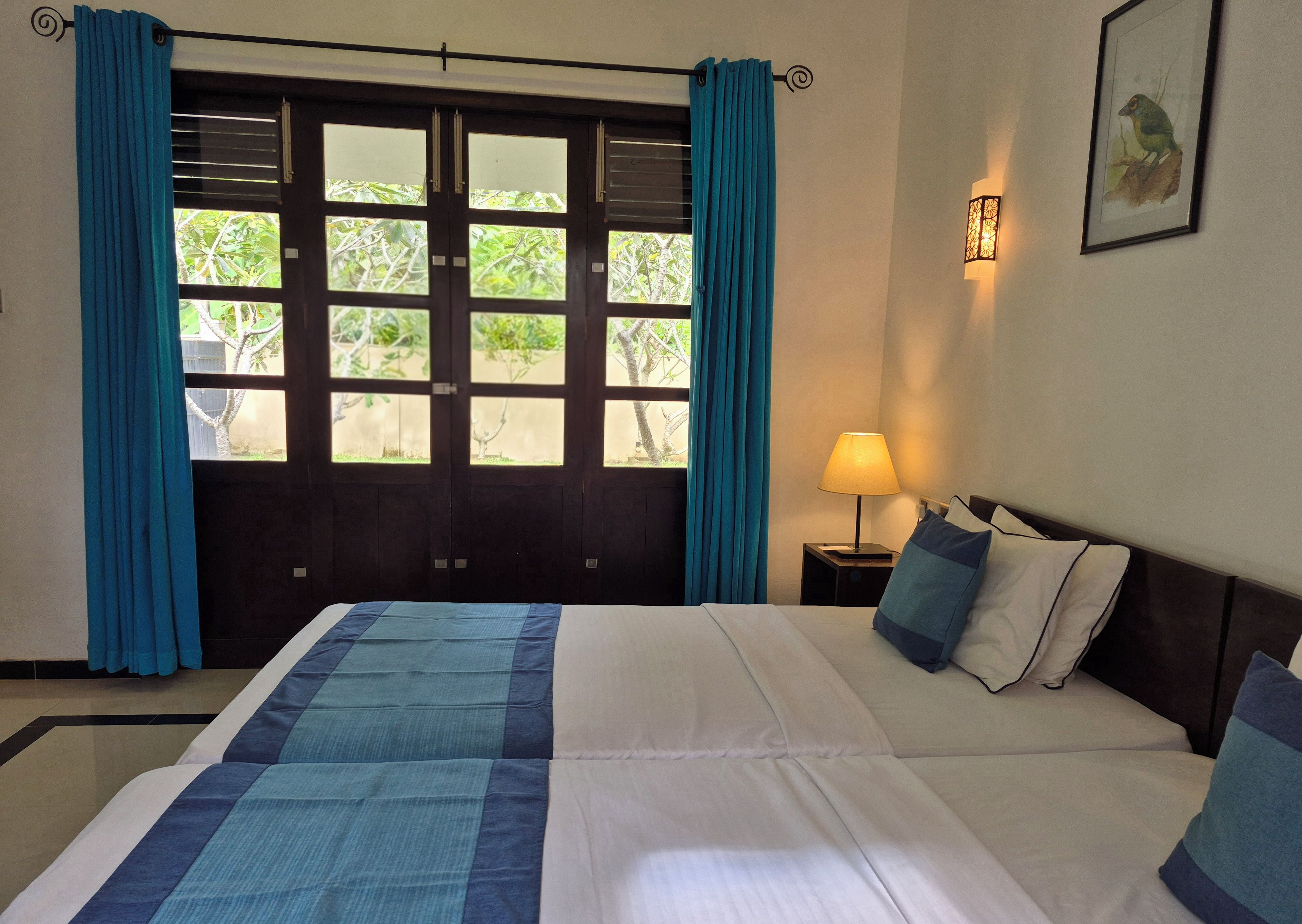 A hotel room with a bed, curtains, a nightstand with a lamp, and a framed picture on the wall.