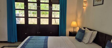 A hotel room with a bed, curtains, a nightstand with a lamp, and a framed picture on the wall.