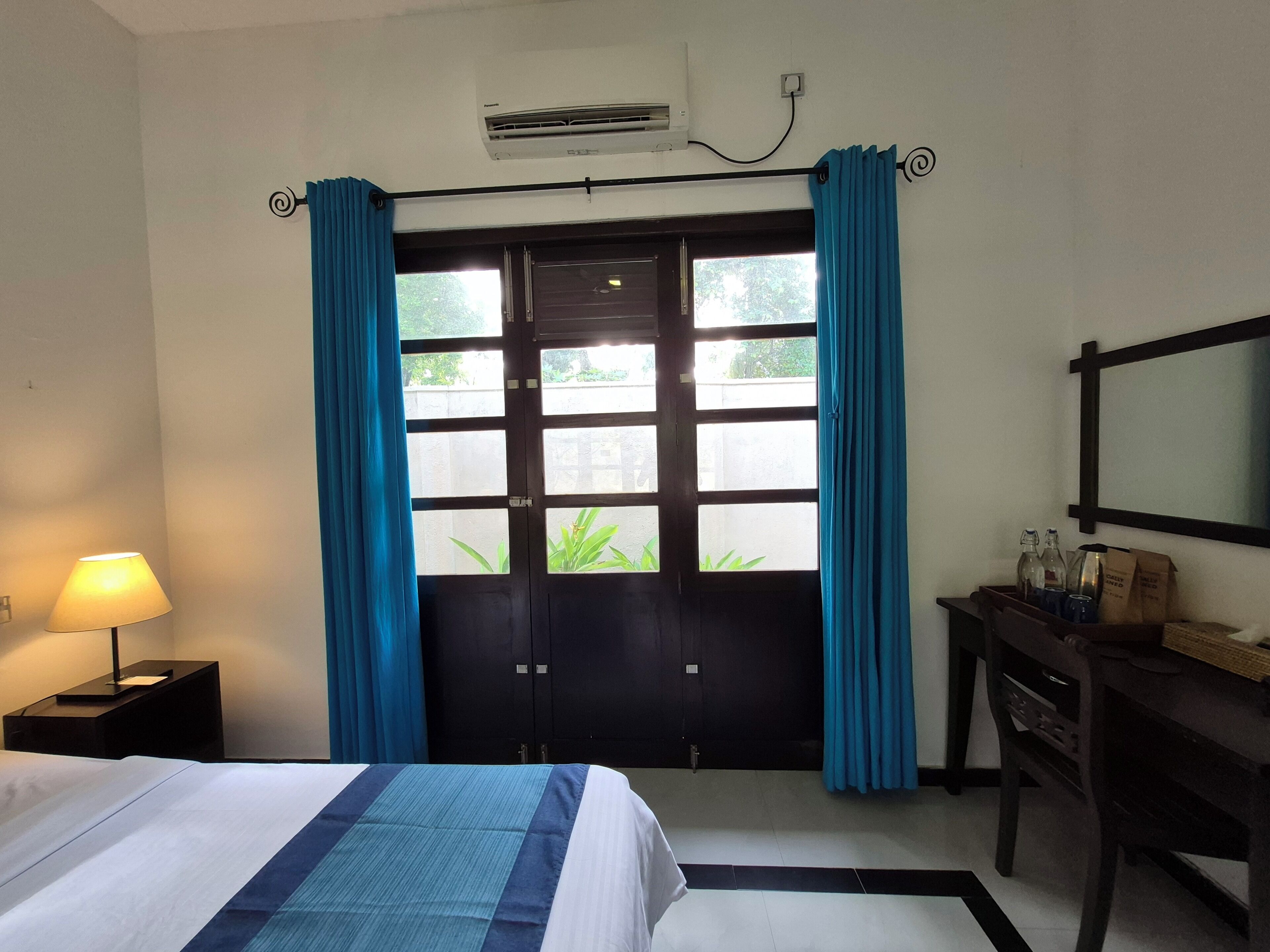 A hotel room with a bed, a desk, a mirror, and a window with curtains.